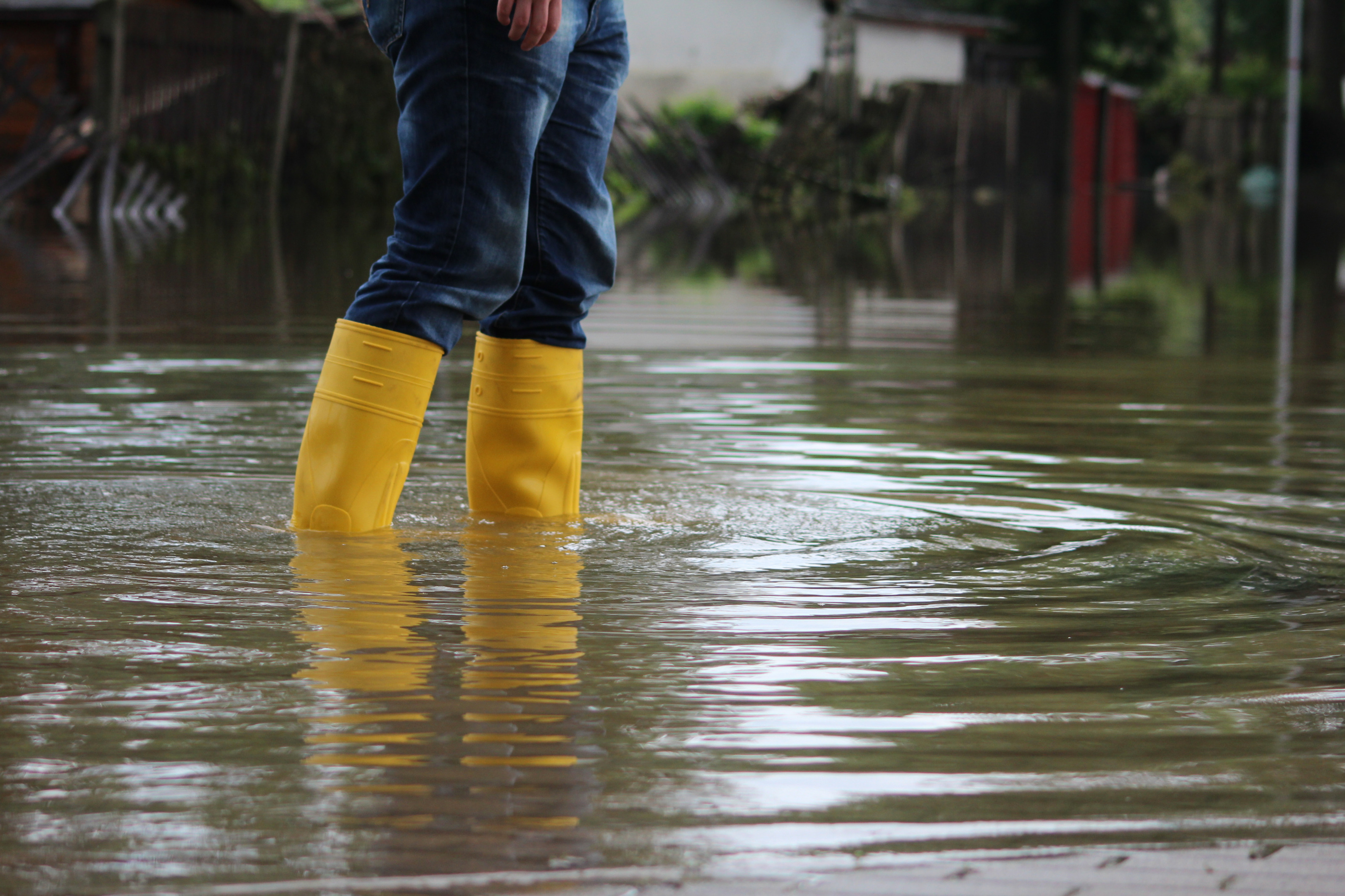 Person in Jeans steht mit gelben Gummistiefeln in tiefem Wasser, Hochwasser