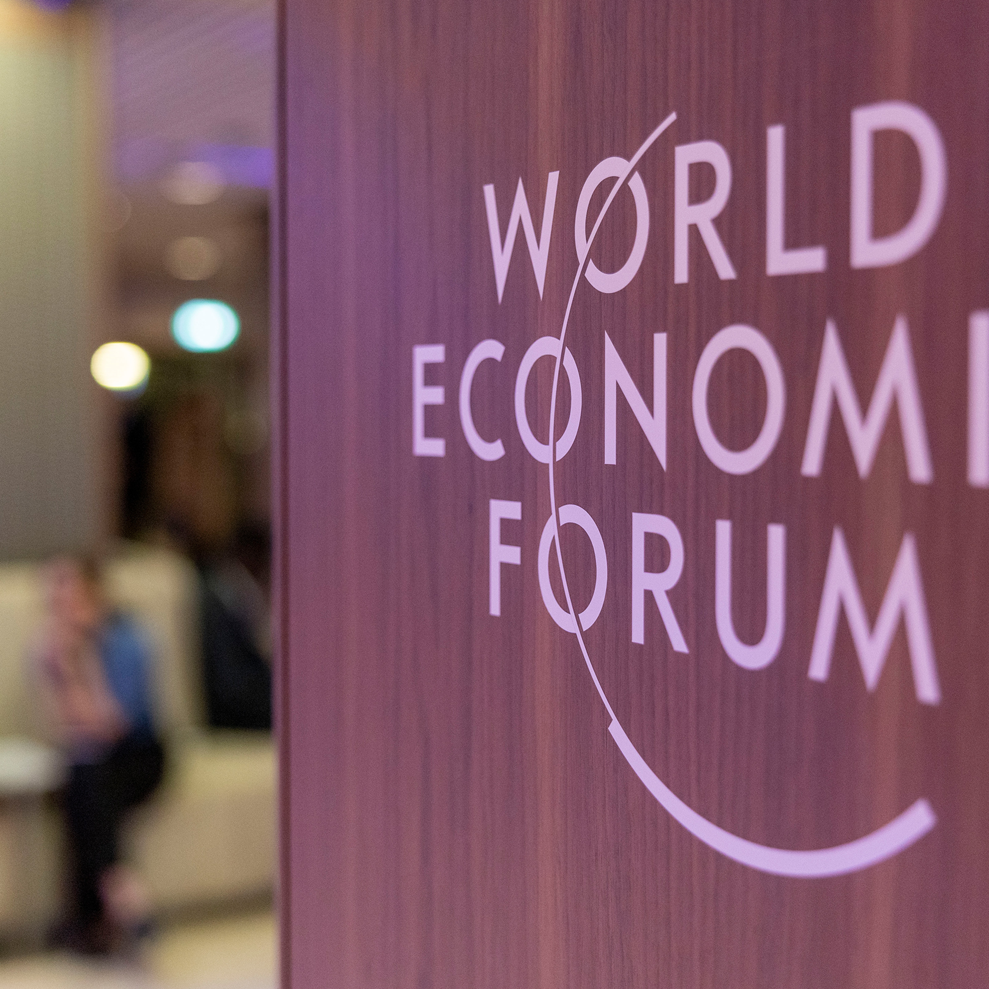 Auf einer Wand steht World Economic Forum. Im Hintergrund sitzen zwei Personen