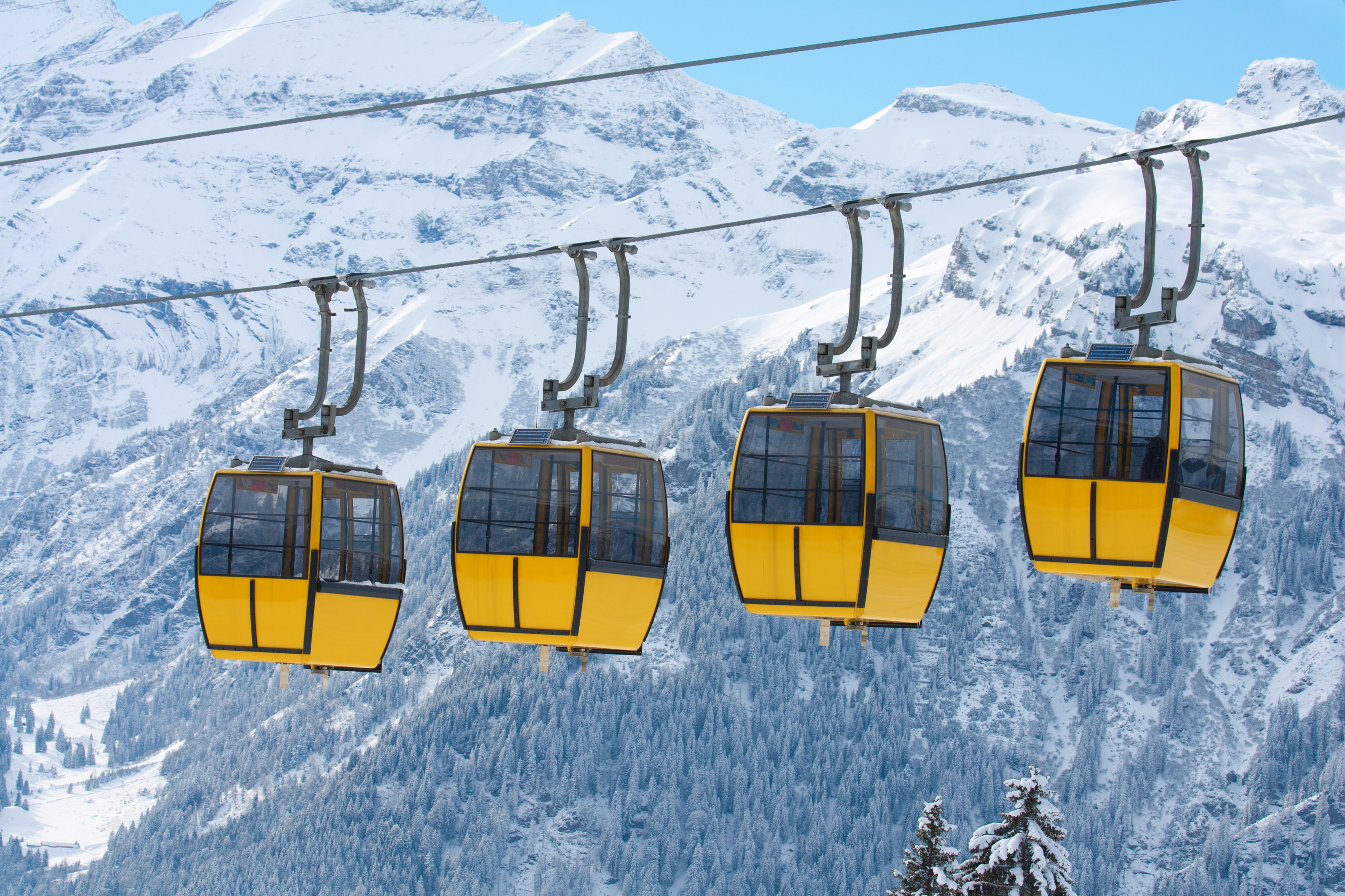 Vier gelbe Seilbahngondeln, im Hintergrund winterliche Berglandschaft