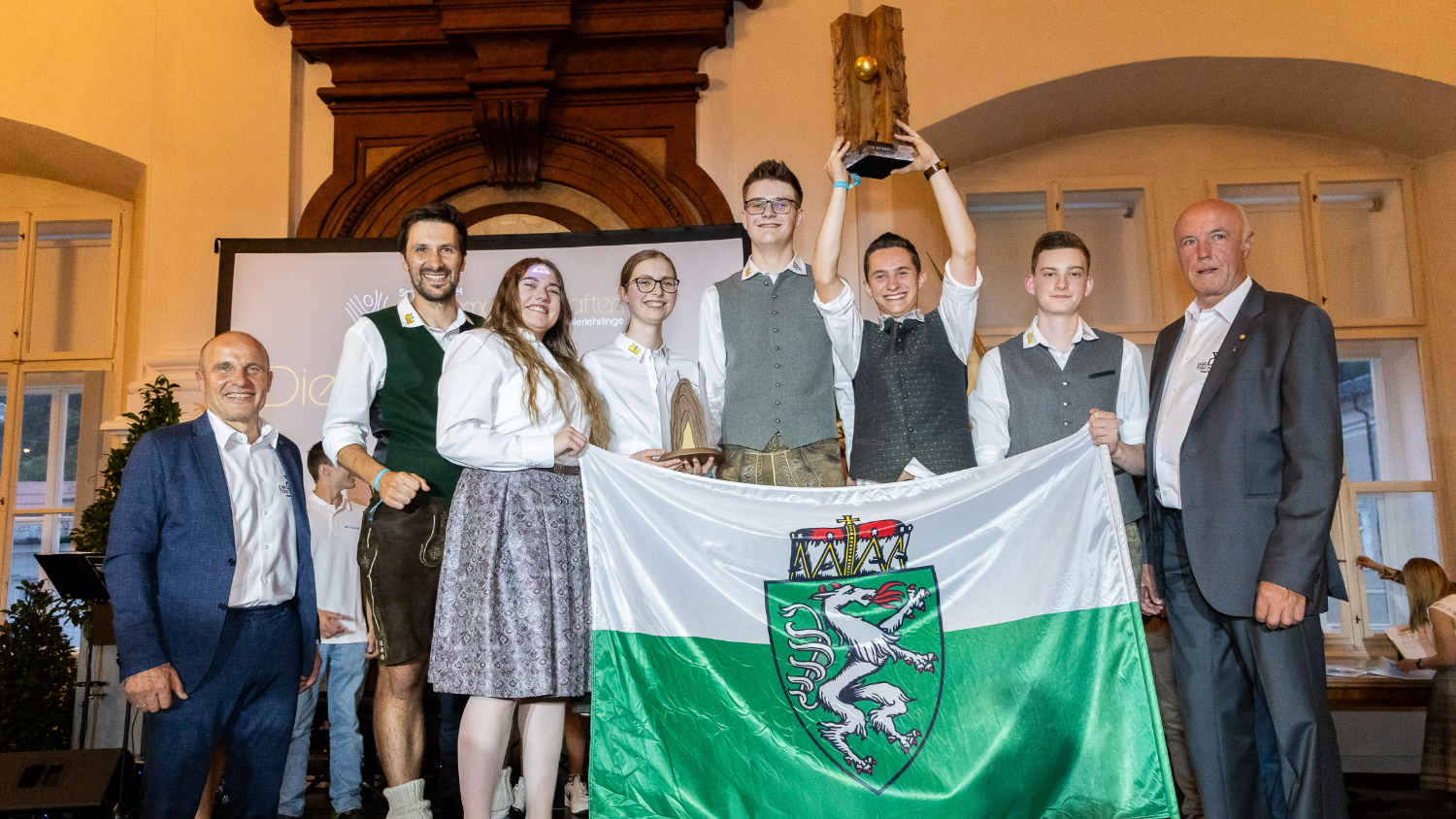 Lehrlinge und Betreuer halten steirische Flagge und Pokal hoch
