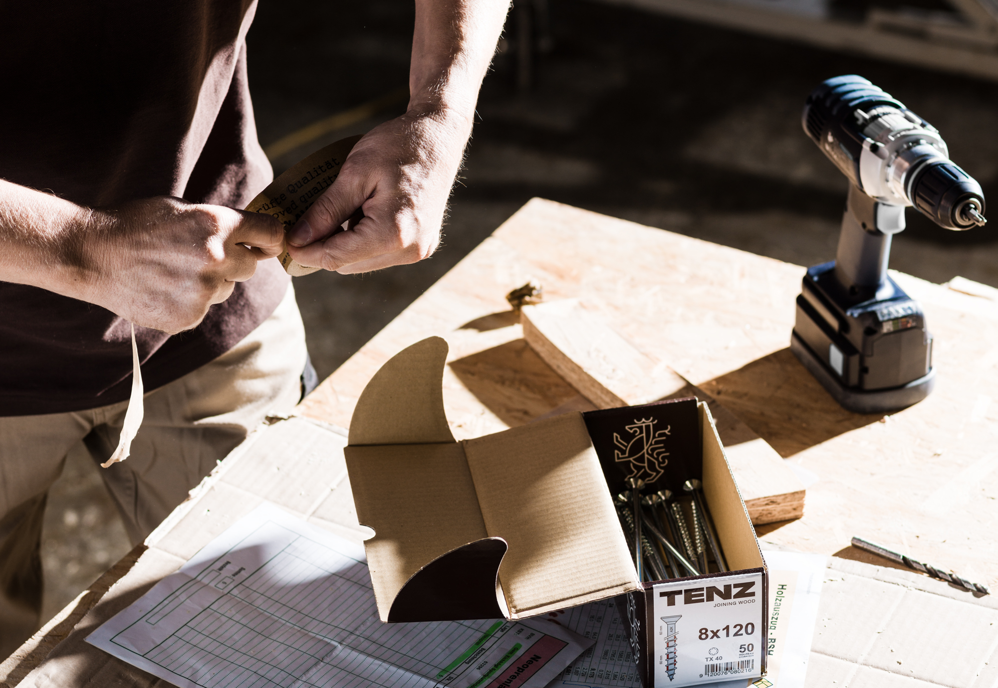 Eine Person hält eine Schraube, daneben sieht man die übersichtlich gestaltete Verpackung