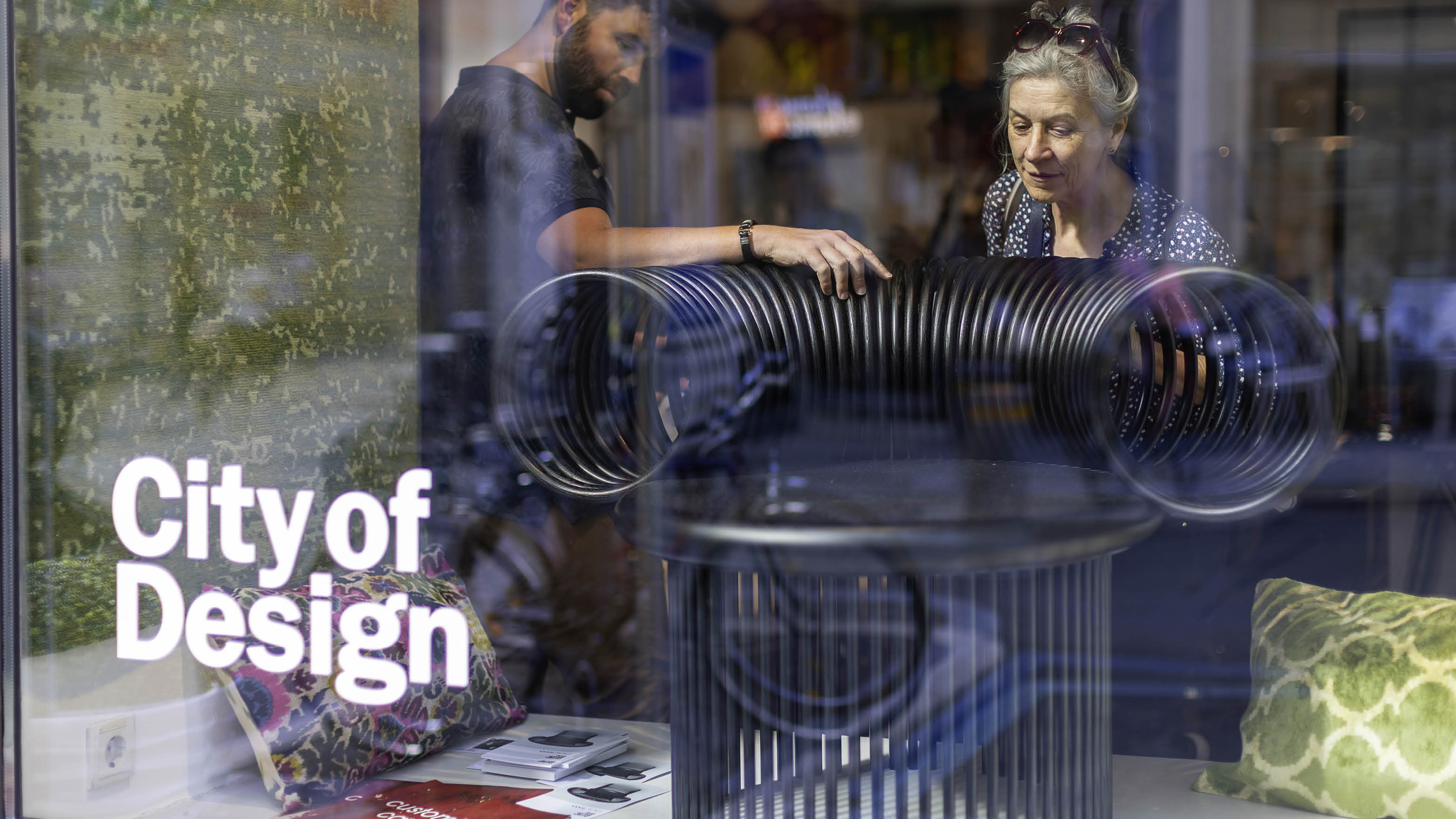 Zwei Personen bewundern in einem Schaufenster ein schwarzes Designobjekt