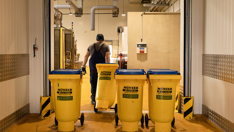 Ein Mann zieht eine gelbe Münzer-Mülltonne, daneben stehen weitere