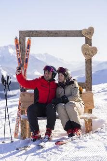 Zwei Skifahrer sitzen auf einer Bank. Rundherum sind Herzen aus Holz