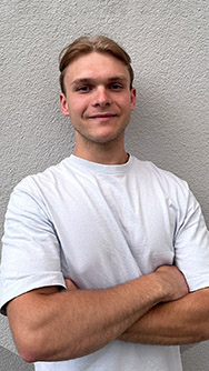 Ein junger Mann mit verschränkten Armen vor einer weißen Wand