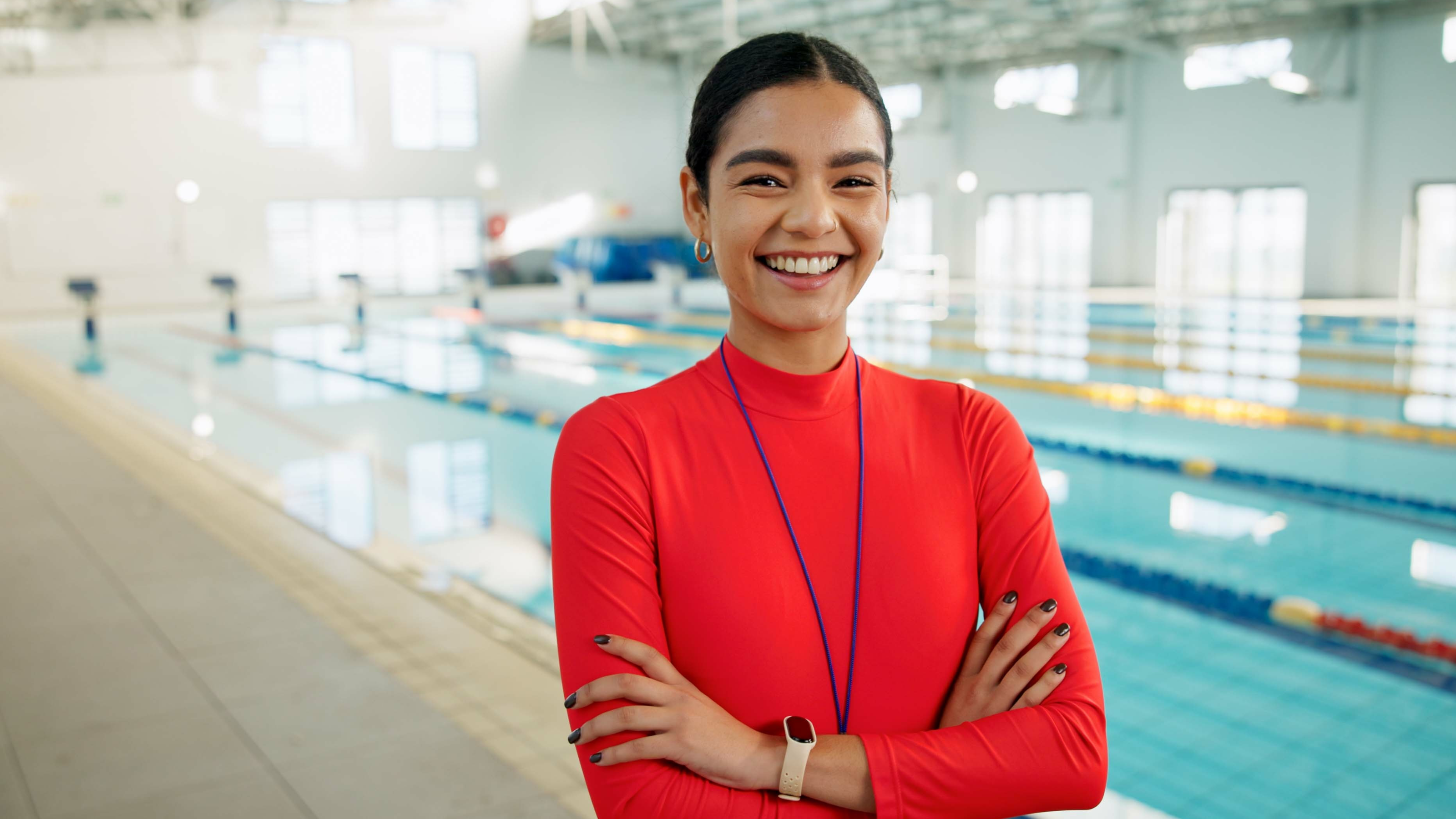 Frau in orangefarbenem Anzug lacht vor einem Indoor-Schwimmbecken 