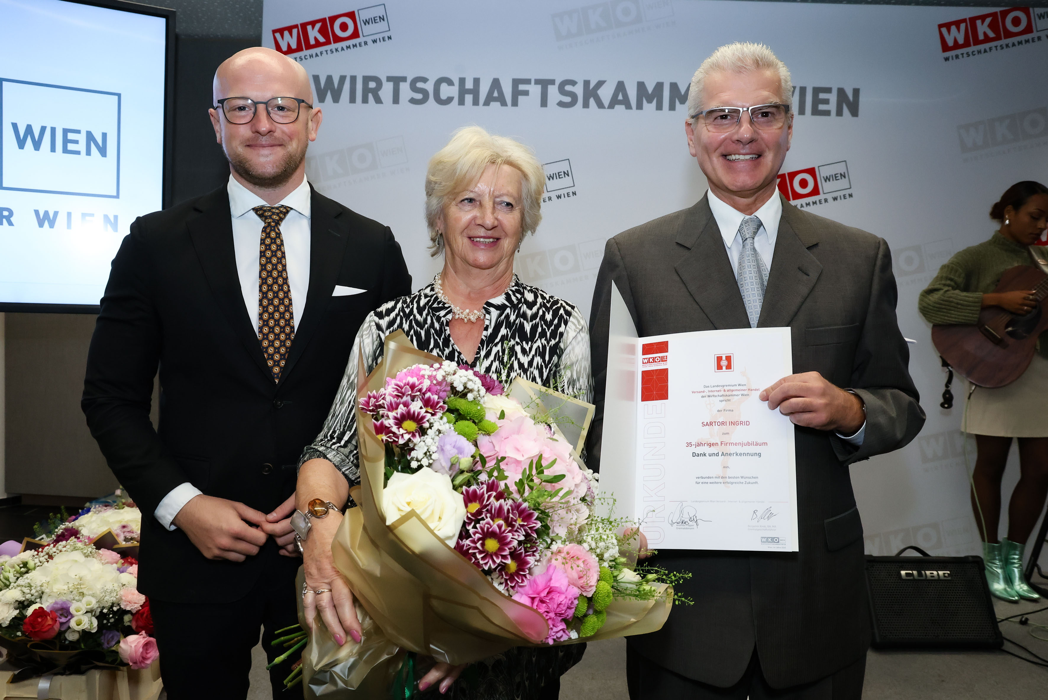 3 Personen vor WK Wien-Wand - in der Mitte eine Person mit Blumen