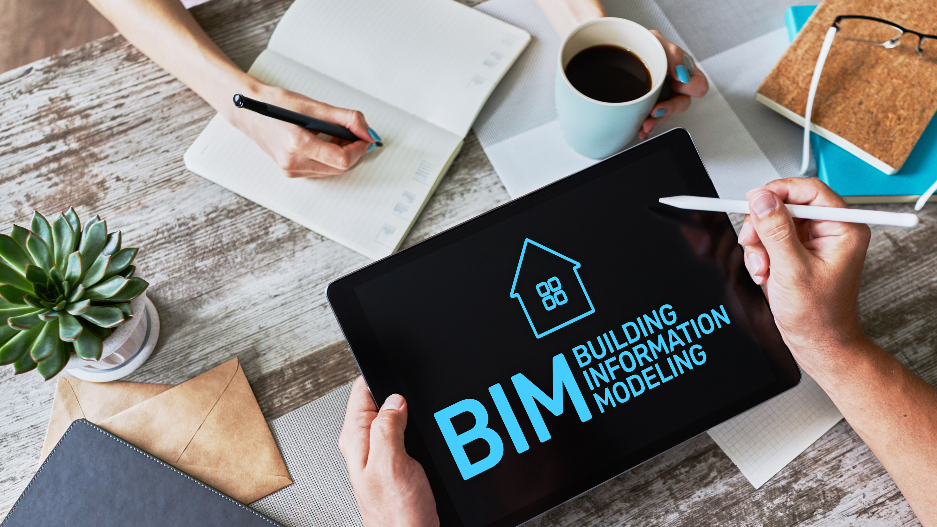 Fokus auf Tablet mit blauer Schrift BIM Building Information Modeling , Tablet wird von Händen gehalten mit Tabletstift über Tisch mit verschiedenen Schreibtischutensilien,